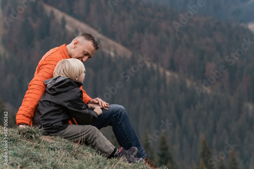Father and his son sit on slope and look at the mountains. Family trekking with children in forest