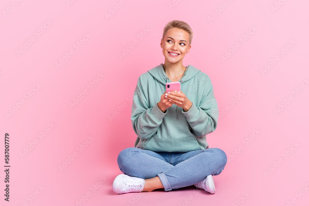 Full length photo of pretty lady influencer sit floor promoting quality samsung iphone look empty space isolated on pink color background Full length photo of pretty lady influencer sit floor promoting quality samsung iphone look empty space isolated on pink color background