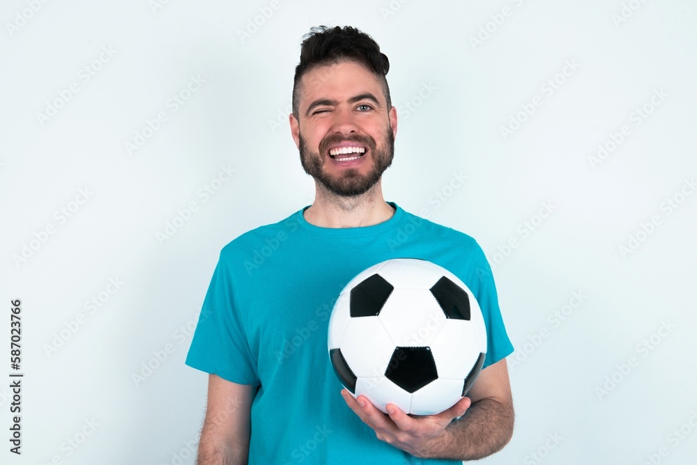 Coquettish Young man holding a ball over white background smiling happily, blinking at camera in a playful manner, flirting with you. Coquettish Young man holding a ball over white background smiling happily, blinking at camera in a playful manner, flirting with you.
