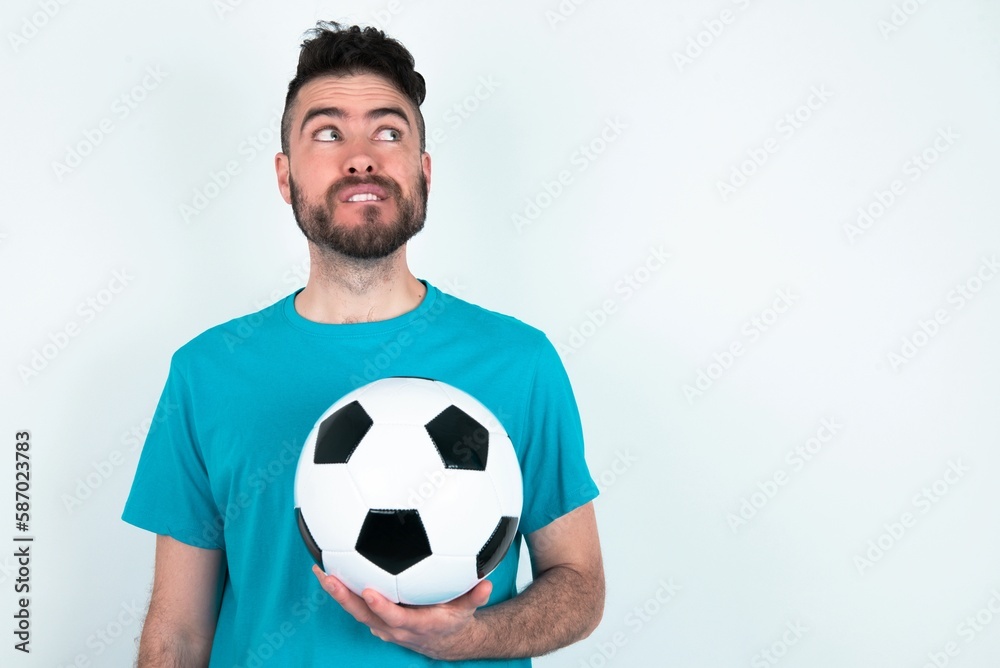 Amazed Young man holding a ball over white background bitting lip and looking tricky to empty space. Amazed Young man holding a ball over white background bitting lip and looking tricky to empty space.