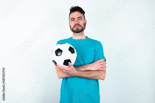 Serious pensive Young man holding a ball over white background feel like cool confident entrepreneur cross hands.