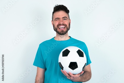 Coquettish Young man holding a ball over white background smiling happily, blinking at camera in a playful manner, flirting with you. © Jihan