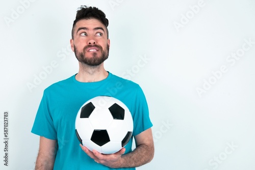 Amazed Young man holding a ball over white background bitting lip and looking tricky to empty space. © Jihan