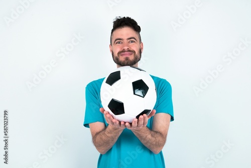Young man holding a ball over white background holding something with open palms, offering to the camera. © Jihan