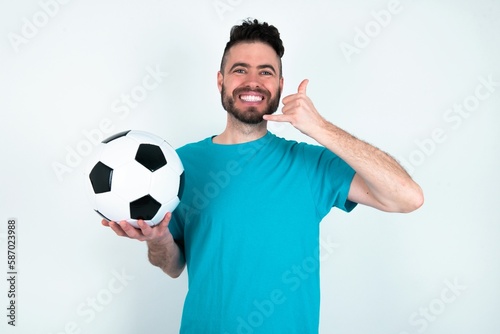 Young man holding a ball over white background smiling doing phone gesture with hand and fingers like talking on the telephone. Communicating concepts.