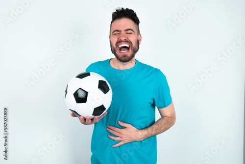 Young man holding a ball over white background smiling and laughing hard out loud because funny crazy joke with hands on body.
