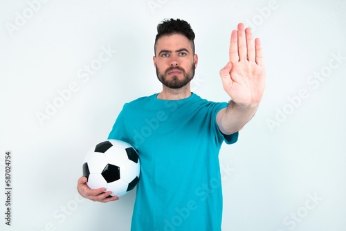 Young man holding a ball over white background doing stop sing with palm of the hand. Warning expression with negative and serious gesture on the face.