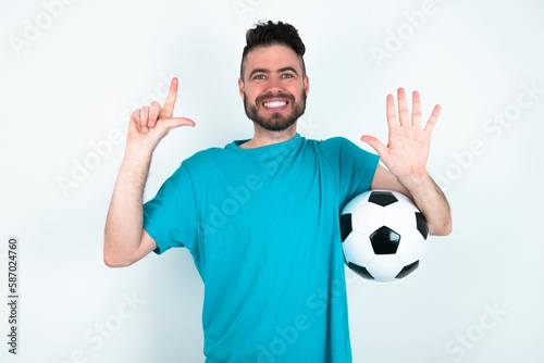 Young man holding a ball over white background showing and pointing up with fingers number seven while smiling confident and happy.