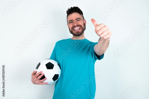 Photography Young man holding a ball over white background approving doing positive gesture with hand, thumbs up smiling and happy for success