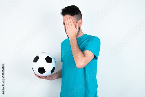 Young man holding a ball over white background Yawning tired covering half face  eye and mouth with hand. Face hurts in pain.