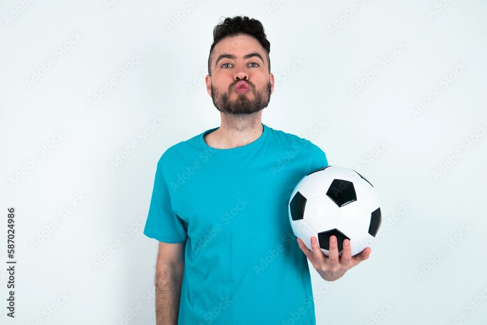 Shot of pleasant looking Young man holding a ball over white background , pouts lips, looks at camera, Human facial expressions