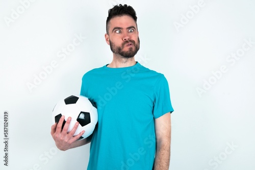 Young man holding a ball over white background making grimace and crazy face, screaming out of control, funny lunatic expressing freedom and wild.