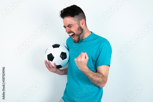 Young man holding a ball over white background very happy and excited doing winner gesture with arms raised, smiling and screaming for success. Celebration concept.