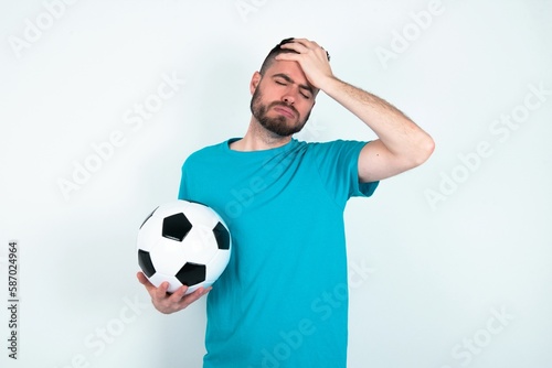 Young man holding a ball over white background suffering from strong headache desperate and stressed because of overwork. Depression and pain concept.