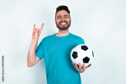 Young man holding a ball over white background doing a rock gesture and smiling to the camera. Ready to go to her favorite band concert. © Jihan