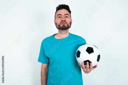 Shot of pleasant looking Young man holding a ball over white background , pouts lips, looks at camera, Human facial expressions