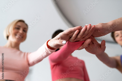 group of young women wearing fitness suits put hands together, team building