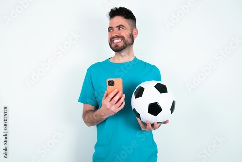 Young man holding a ball over white background hold telephone hands read good youth news look empty space advert