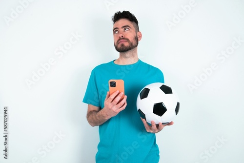 Young man holding a ball over white background holds telephone hands reads good youth news look empty space advert