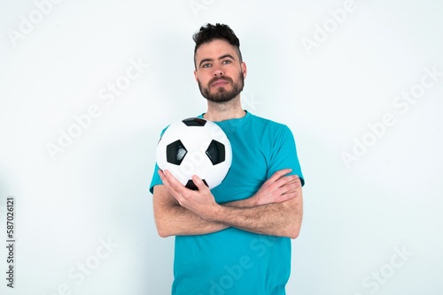 Self confident serious calm Young man holding a ball over white background stands with arms folded. Shows professional vibe stands in assertive pose. © Jihan