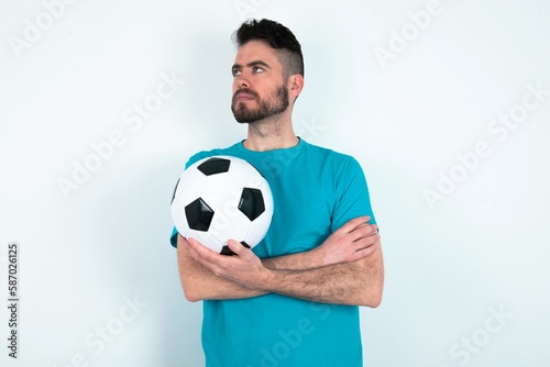 Charming thoughtful Young man holding a ball over white background stands with arms folded concentrated somewhere with pensive expression thinks what to do