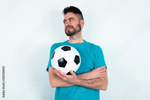Pleased Young man holding a ball over white background keeps hands crossed over chest looks happily aside