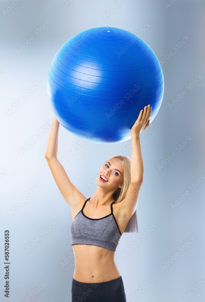 Portrait of happy excited blond woman in sportswear with fitball, standing on blurred modern gym center background. Fitness, exercising and fit gym concept. Portrait of happy excited blond woman in sportswear with fitball, standing on blurred modern gym center background. Fitness, exercising and fit gym concept.