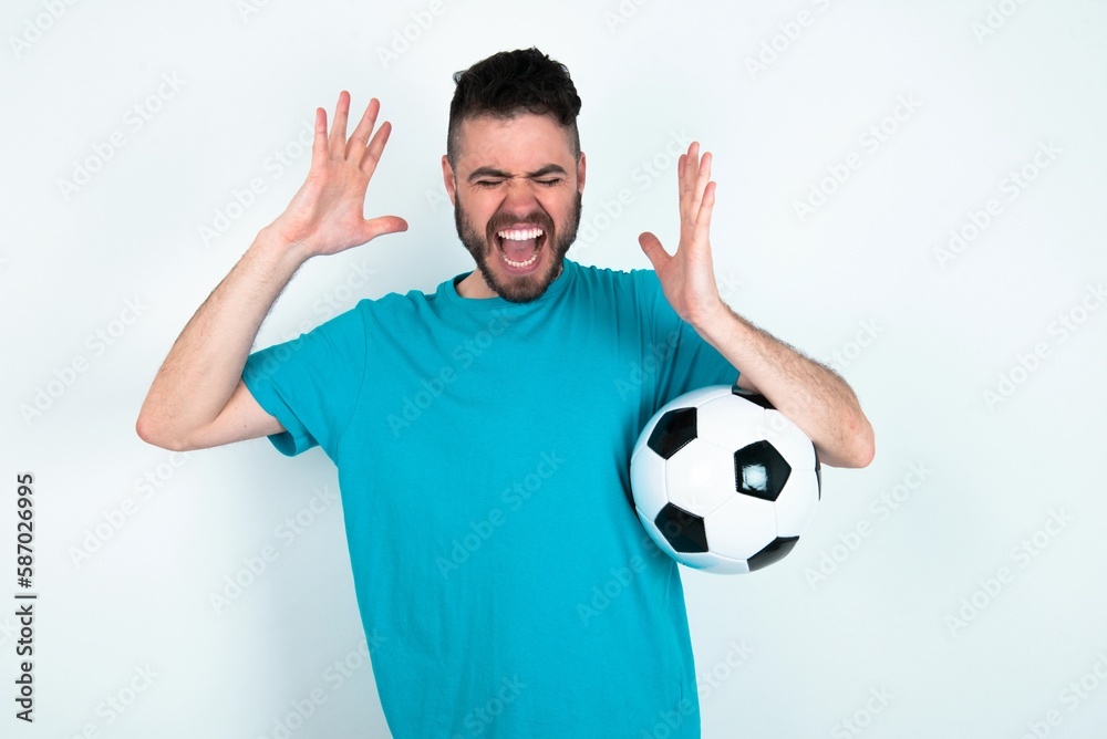 Young man holding a ball over white background goes crazy as head goes around feels stressed because of horrible situation