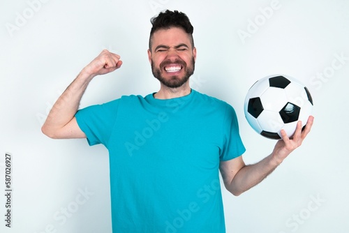 Strong powerful Young man holding a ball over white background toothy smile, raises arms and shows biceps. Look at my muscles!