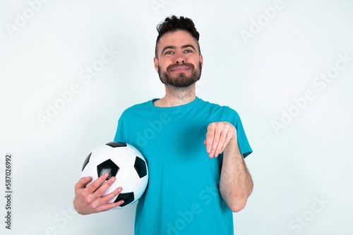 Young man holding a ball over white background makes bunny paws and looks with innocent expression plays with her little kid