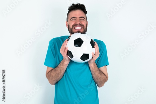 Young man holding a ball over white background grins joyfully, imagines something pleasant, copy space. Pleasant emotions concept. © Jihan