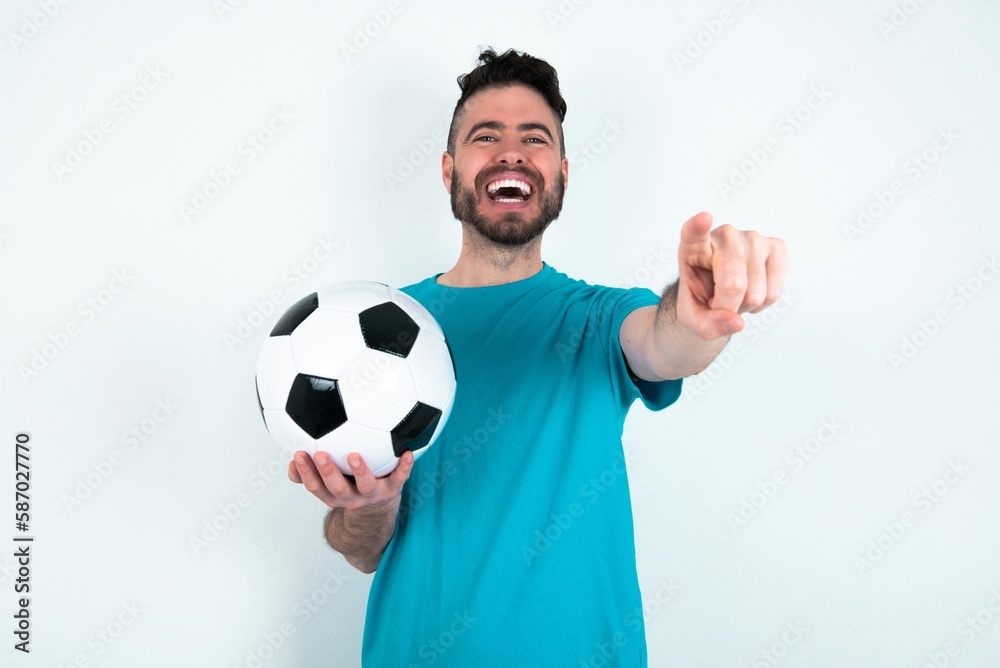 Young man holding a ball over white background cheerful and smiling poiting at camera Young man holding a ball over white background cheerful and smiling poiting at camera