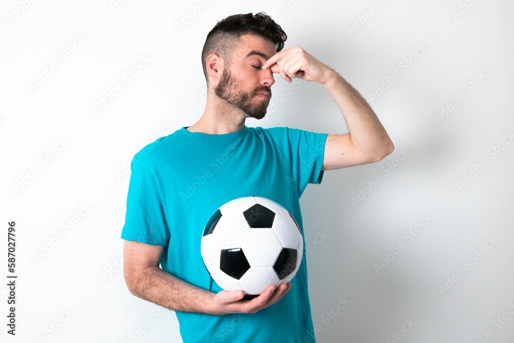 Sad Young man holding a ball over white background suffering from headache holding hand on her face