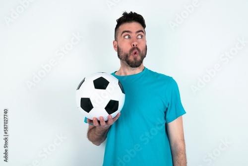 Shocked Young man holding a ball over white background look empty space with open mouth screaming: Oh My God! I can't believe this.
