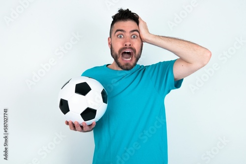 Cheerful overjoyed Young man holding a ball over white background reacts rising hands over head after receiving great news.