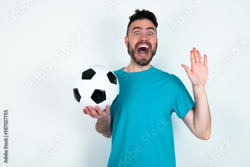 Delighted positive Young man holding a ball over white background opens mouth  and arms palms up after having great result © Jihan