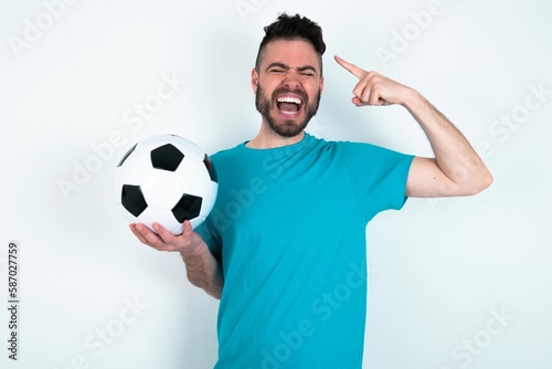 Photo of crazy Young man holding a ball over white background screaming and pointing with fingers at hair closed eyes