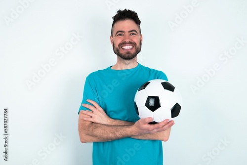 Portrait of charming Young man holding a ball over white background standing confidently smiling toothily with hands folded