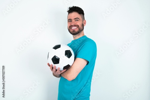 Portrait of Young man holding a ball over white background standing with folded arms and smiling © Jihan
