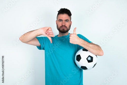 Young man holding a ball over white background showing thumb up down sign