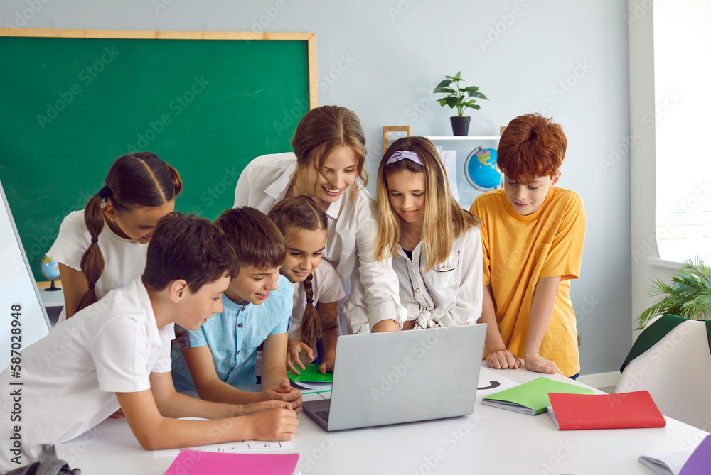 Smart children pupil boys and girls stand in front of laptop with woman teacher and view media material or online presentation during lesson in primary school classroom. Curiosity, education - obrazy, fototapety, plakaty 