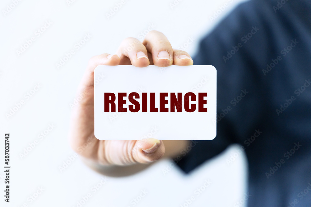 Resilence text on blank business card being held by a woman's hand with blurred background. Business concept about reslience. Resilence text on blank business card being held by a woman's hand with blurred background. Business concept about reslience.