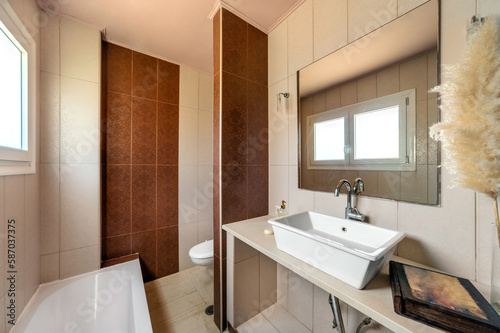 Modern bathroom design in light and beige colors. Tiled walls  white bowl sink  toilet  small window.