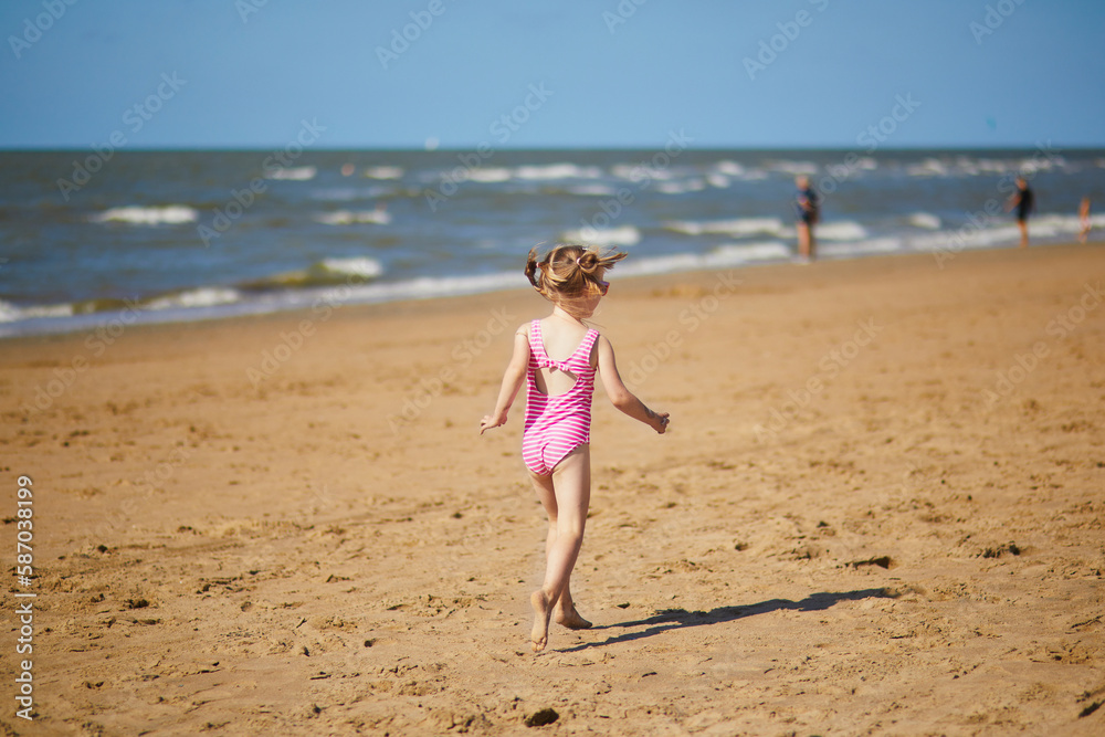 Preschooler girl having fun on the sand beach at sea coast in Noordwijk, the Netherlands