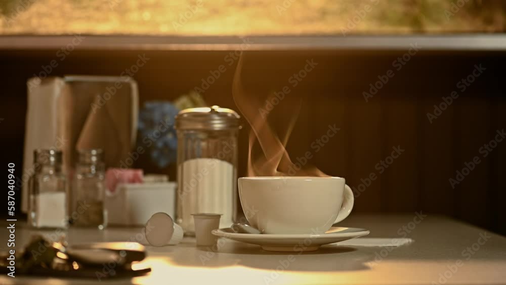 A steaming hot cup and saucer of coffee with steam rising as the light from the sun rises through the dirty window of a diner. A steaming hot cup and saucer of coffee with steam rising as the light from the sun rises through the dirty window of a diner.