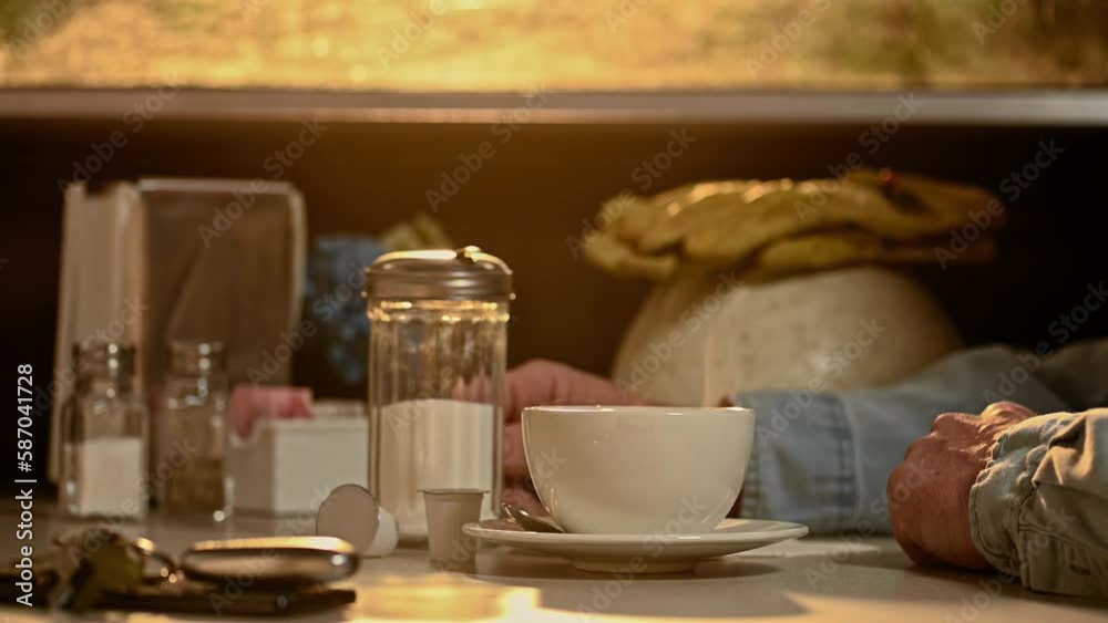 A construction worker stirring his steaming hot cup and saucer of coffee with steam rising as the light from the sun rises through the dirty window of a diner. A construction worker stirring his steaming hot cup and saucer of coffee with steam rising as the light from the sun rises through the dirty window of a diner.