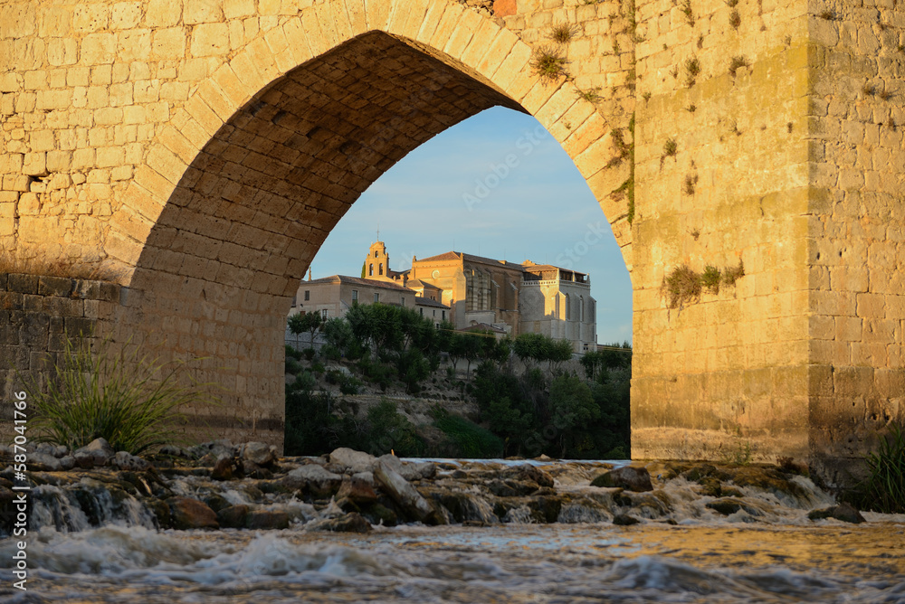 View at water level and through an arch of the medieval stone bridge in Tordesillas-Spain, in the background can be seen the Real Convento de Santa Clara, a national heritage monument.
