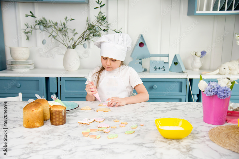 little cute funny smiling girl wearing a white chef's hat and uniform holding decorating easter cake in the blue and white kitchen with easter decoration little cute funny smiling girl wearing a white chef's hat and uniform holding decorating easter cake in the blue and white kitchen with easter decoration