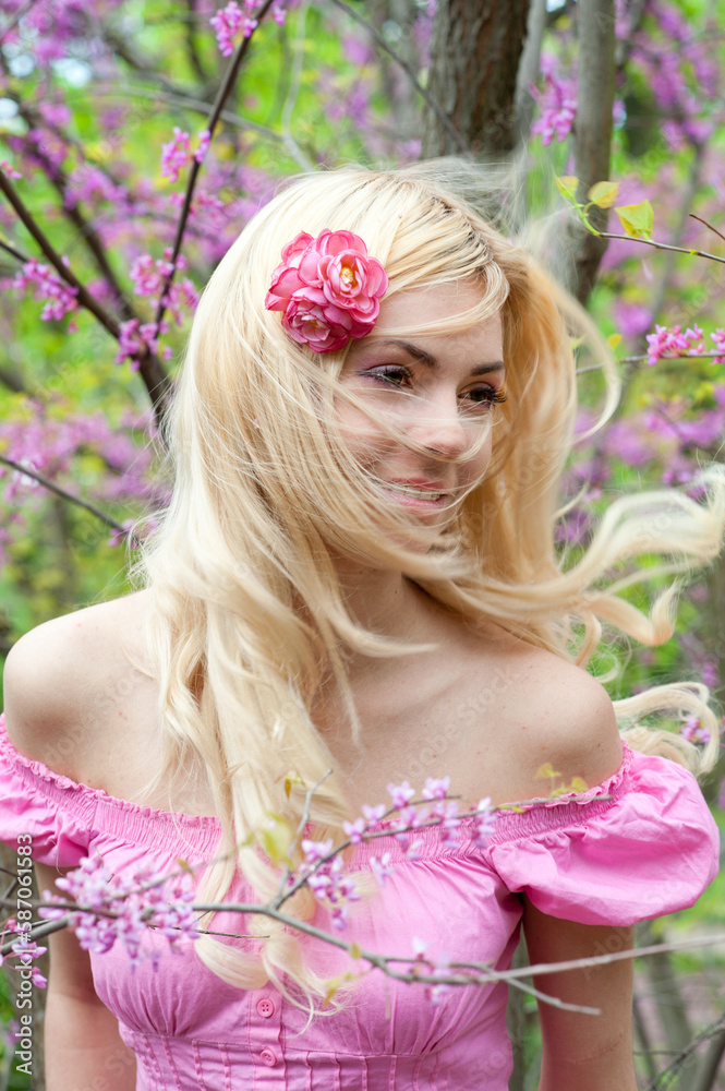 Fototapeta premium Pretty happy blonde fluffy hairs woman posing in spring blooming park
