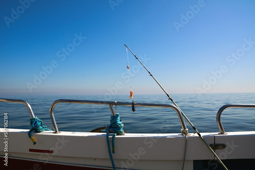 A spinning rod for catching fish is strung on the railing of a fishing boat against the background of the blue sea and sky